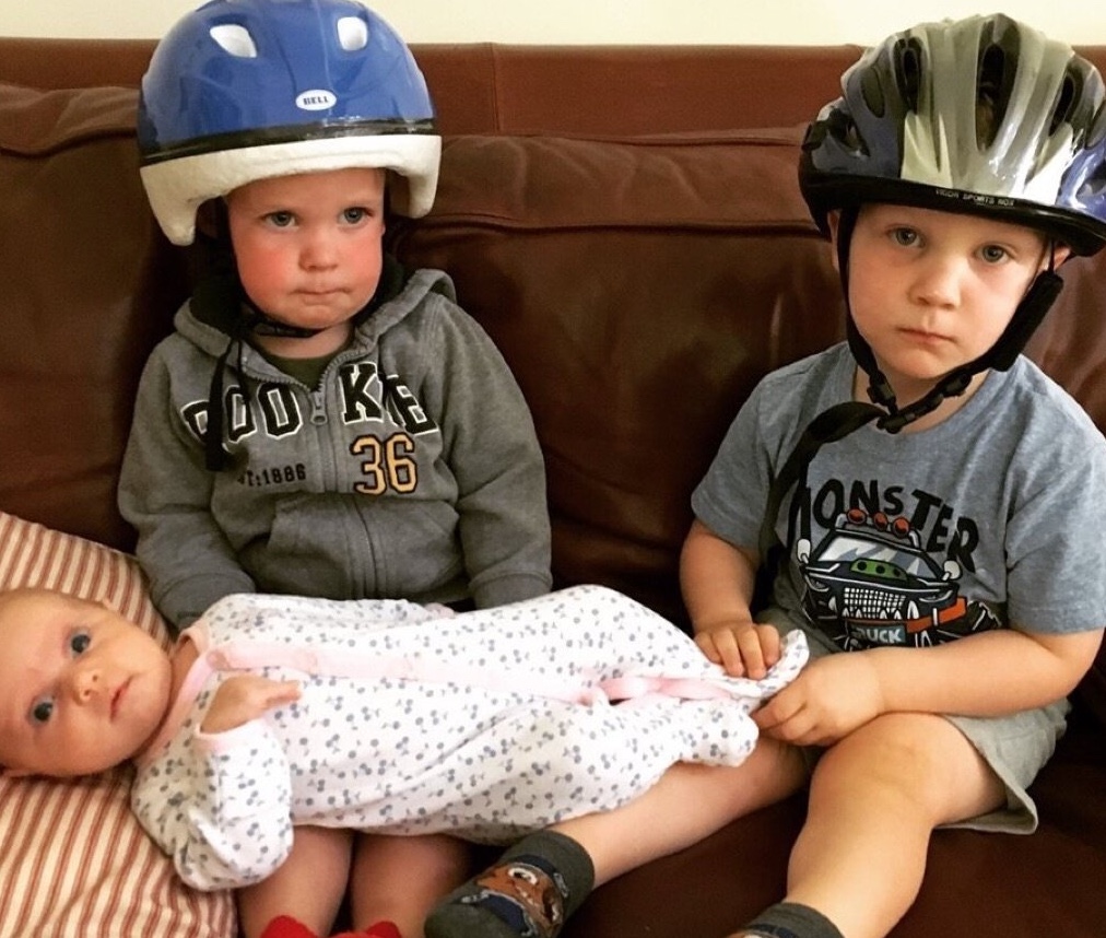 Three young children, two in bike helmets and one baby