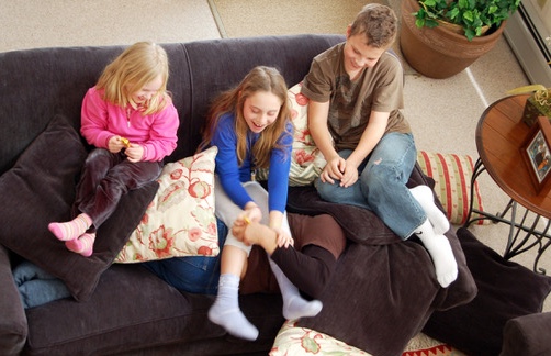 Morgan (hand peeking out), Noah, Julia, and Claire roughhousing on a couch