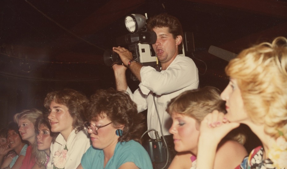 Ross filming with a shoulder camera above a crowd
